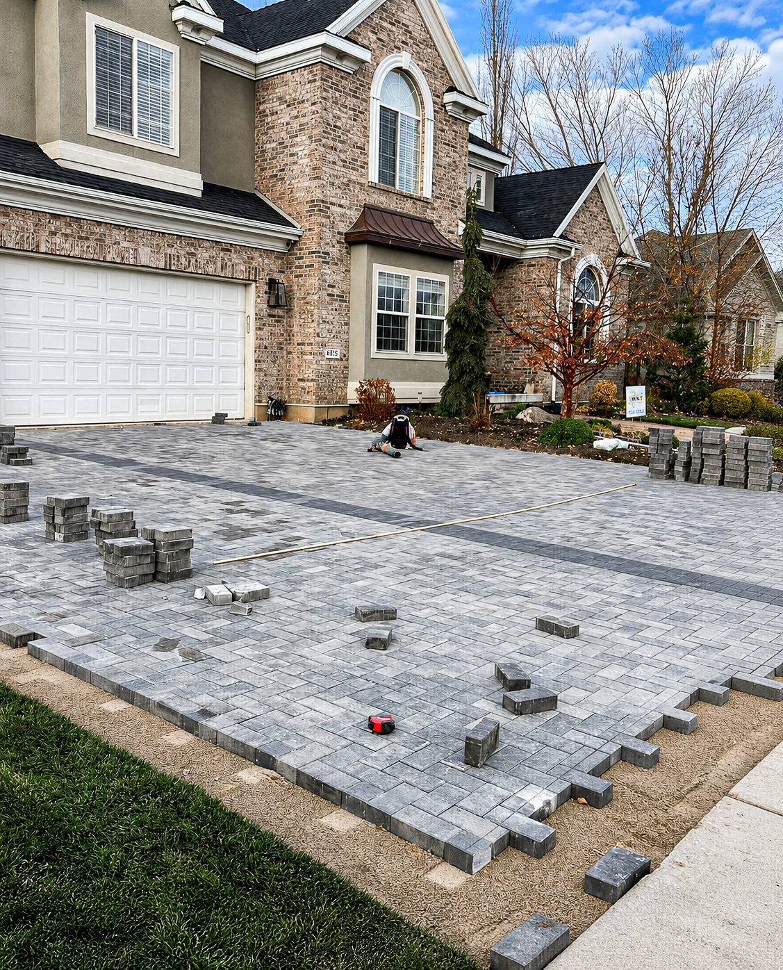 Empire Pavers crew installing a grey paver driveway with stacks of pavers on site, driveway project in South Jordan, UT