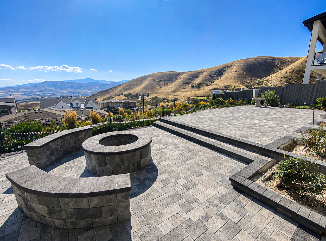 Stone paver patio with a circular fire pit and curved seat wall overlooking Utah foothills, fire pits & features by Empire Pavers in Utah