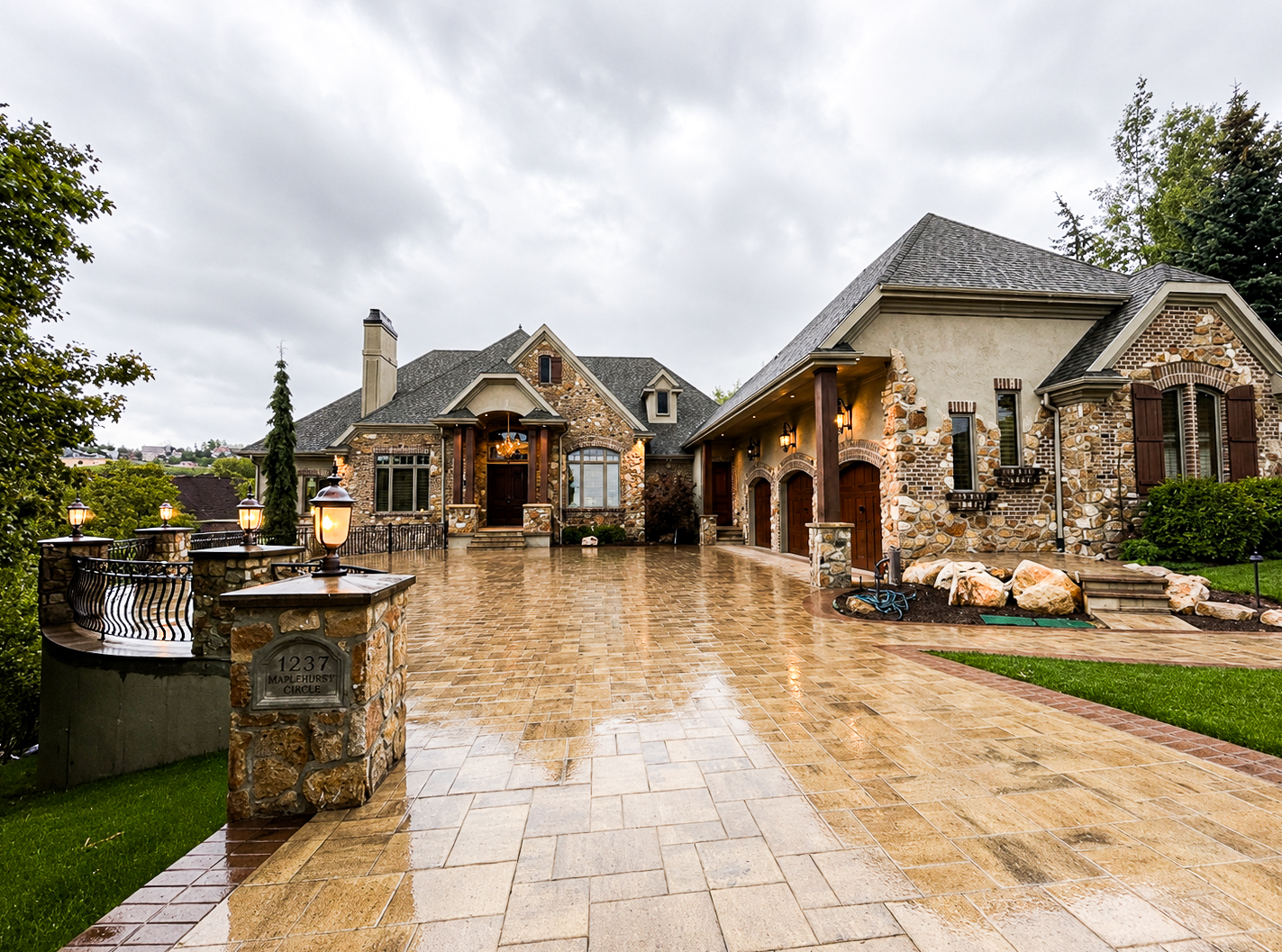 Tan paver driveway leading to a luxury Utah home with stone siding and multiple garage bays, paver driveways by Empire Pavers in Utah